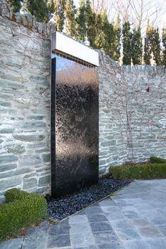 a black water fountain sitting next to a stone wall