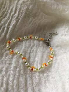 a white bracelet with multicolored beads and a silver cross on the clasp is laying on a white sheet