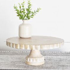 a white vase sitting on top of a wooden table next to a plant in it