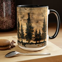 there is a coffee mug with trees on it next to some spoons and a cookie