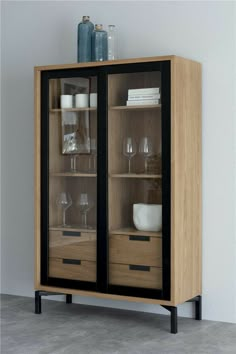 a wooden cabinet with glass doors and black trim on the bottom, in front of a white wall