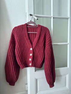 a red cardigan sweater hanging on a white door