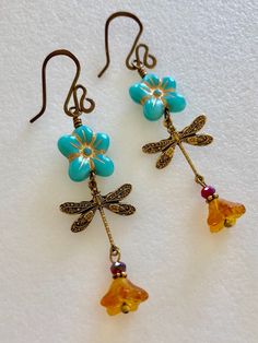 "Adorable turquoise blue Czech glass puffed daisies with topaz yellow bellflowers and vintage bronze stamped dragonfly charms. Matte turquoise 14 mm Czech glass puffy 5 petal flowers are etched with metallic gold and wire wrapped in vintage bronze with 6 x 9 mm translucent topaz yellow bellflowers accented with tiny burnt orange crystals. Lightweight dangles hang on handmade and hammered vintage bronze ear wires. Total drop length is 2 1/2\"." Whimsical Blue Jewelry With Flower Charm, Vintage Turquoise Flower Earrings, Handmade Blue Whimsical Flower Earrings, Whimsical Handmade Blue Flower Earrings, Whimsical Turquoise Nickel-free Earrings, Vintage Turquoise Dangle Flower Earrings, Nickel Free Turquoise Flower Earrings, Turquoise Nickel Free Flower Earrings, Blue Whimsical Dangle Flower Earrings