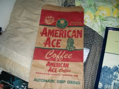 an american ace coffee bag sitting on top of a bed next to pillows and pictures