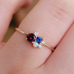 a close up of a person's hand wearing a ring with an oval blue and red stone