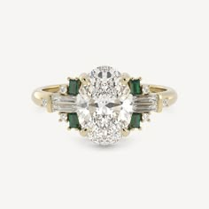 an oval diamond and emerald engagement ring with two baguettes on the side, set in yellow gold