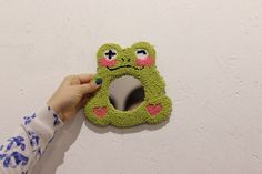 a person holding up a green frog shaped mirror to the wall with it's eyes open