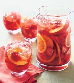 several glasses filled with red liquid and sliced oranges next to each other on a table