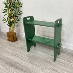 a green bench next to a potted plant on the floor in front of a white wall