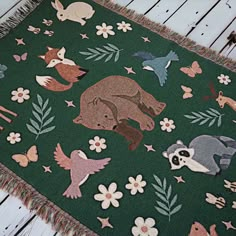 a green rug with animals on it and flowers around the edges is laying on a white wooden floor