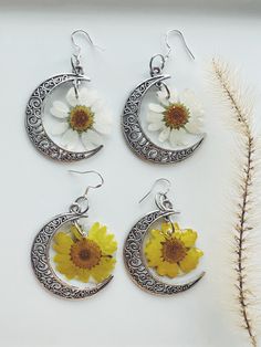 three earrings with flowers on them sitting next to a white flower and silver ear wires