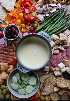 a platter filled with meats, vegetables and dip surrounded by other food items