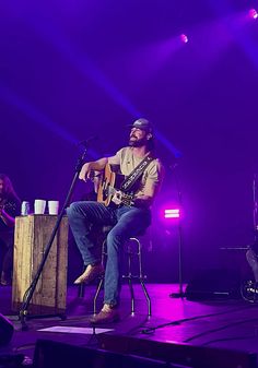 a man sitting on top of a stool next to a microphone and an acoustic guitar