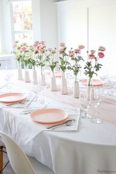 the table is set with pink flowers in vases and plates on top of it