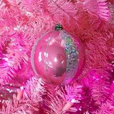 a pink christmas ornament hanging from the side of a tree with purple tinsel