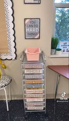 a metal cart with lots of books on it in front of a window and some pictures