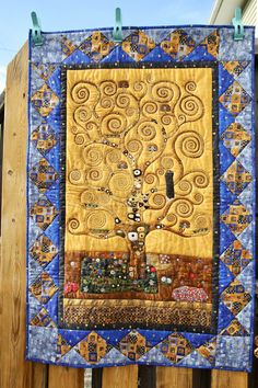 the tree of life quilt is hanging on a wooden fence with blue and yellow accents