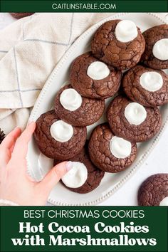 the best christmas cookies with marshmallows are on a white platter and there is a hand reaching for one