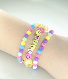 "♥ Pretty and cheery beaded bracelet set.  Pink Set ♥ Two round plastic bead bracelets in blue, pink, purple, green, yellow, and white. ♥ One pink seed beads, yellow stars, pink smiley faces, and letter beads spelling \"SMILE\" Yellow Set ♥ Two round plastic bead bracelets in blue, pink, purple, green, yellow, and white. ♥ One yellow seed beads, pink stars, yellow smiley faces, and letter beads spelling \"SMILE\" ♥ Stack the bracelets or wear them separately.    ♥ They are made out of elastic co Cute Beaded Plastic Stretch Bracelet, Multicolor Charm Bracelet With Round Beads For Birthday, Plastic Beaded Friendship Bracelets, Plastic Letter Beads Bracelets As Gift, Cute Plastic Bracelets With Letter Beads, Colorful Beads Plastic Bracelets For Birthday, Cute Beaded Bracelets With Letter Beads, Playful Plastic Bracelets With Letter Beads, Beaded Bracelets With Heart Beads For Birthday