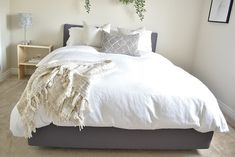 a bed with white linens and pillows in a bedroom next to two plants on the wall