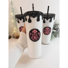 three starbucks cups with black and pink designs on them are being held by a person