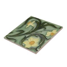 a green and yellow tile with white flowers on it's side, against a white background