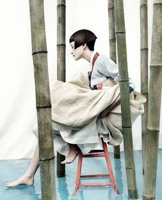 a person sitting on a chair in front of some tall bamboo trees with their legs spread out