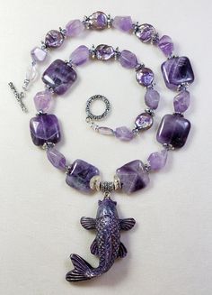 Gorgeous handmade polymer clay purple Koi Fish pendant made by Massachusetts artist Stacey. I gave this purple Koi Fish a necklace of genuine Amethyst beads, (squares and irregular chunks), purple colored freshwater pearls, 2 light Amethyst ovals (near clasp), tiny purple Swarovski crystal bicone beads and pewter spacers and toggle clasp, (cadmium and lead free). This necklace is 20 inches long and the Koi pendant drops down from the necklace approx. 2.5 inches. One Of A Kind I can send it gift Handmade Purple Rectangular Necklace, Purple Rectangular Amethyst Necklaces, Rectangular Purple Amethyst Necklaces, Purple Rectangular Amethyst Necklace, Polymer Clay Koi Fish, Clay Koi Fish, Purple Koi Fish, Fish Necklace, Fish Pendant