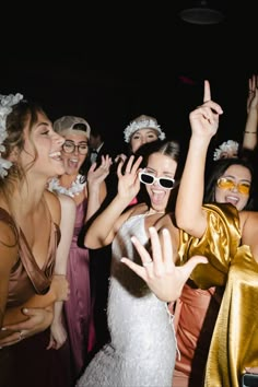 a group of young women dressed in evening wear dancing together at a party with their hands up