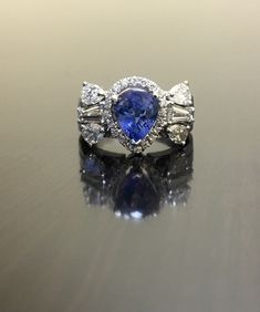 DeKara Designs Collection Beautiful Modern/Art Deco Ceylon Blue Sapphire and Diamond Ring Metal- 18K White Gold, 750. Stones- 1 Pear Shape Ceylon Blue Sapphire 2.25 Carats, 2 Tapered Baguette Diamonds F-G color VS1 clarity 0.60 Carats, 4 Pear Shape Diamonds F-H Color VS2 Clarity 1.05 Carats, 20 Round Diamonds G Color VS2 Clarity 0.25 Carats. 1.90 Total Carats of Diamonds. Art Deco Inspired 18K White Gold Ceylon Blue Sapphire Diamond Engagement Ring. There is a three prong set pear shape pear sha Blue Multi-stone Diamond Ring In 14k White Gold, Trillion Cut Tanzanite Rings For Wedding, Heirloom Blue Diamond Ring In 14k White Gold, Sapphire Pear-shaped Rings With Halo Setting, Blue Sapphire Ring With Multi-stone Baguette Cut, Blue Tanzanite Ring With Trillion Cut, Blue Sapphire Multi-stone Baguette Ring, Exquisite Tanzanite Wedding Rings, Gia Certified Baguette Cut Tanzanite Ring