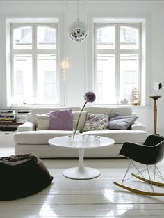 a living room filled with furniture and large windows next to a white floored area