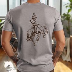 a man wearing a t - shirt with a drawing of a cowboy riding a horse