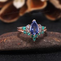 a blue and green ring sitting on top of a piece of wood with flowers in the background