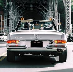 the back end of a silver mercedes benz roadster driving down a city street in front of a bridge