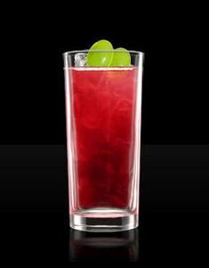 a tall glass filled with red liquid and an apple on the rim, against a black background