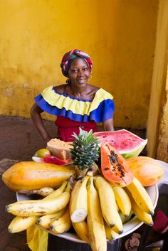 a woman sitting in front of a bowl full of bananas, watermelon and pineapple