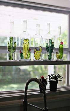 several glass bottles with cactus designs are on a window sill next to a potted plant