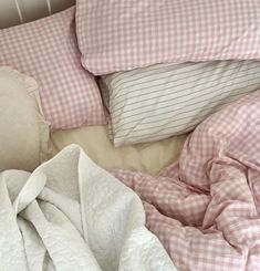 an unmade bed with pink gingham sheets and pillows