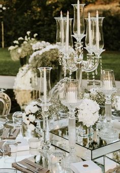 a table topped with lots of glass vases filled with white flowers and greenery