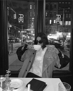 a woman sitting at a table drinking from a cup