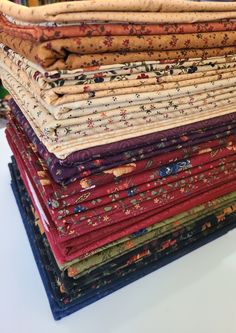 a stack of different colored fabrics sitting on top of a white tablecloth covered surface