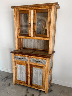 an old wooden hutch with glass doors and wood panels on the front, sitting against a white wall