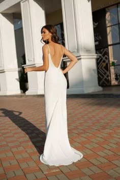 a woman in a white dress is standing on a brick walkway and looking back at the camera