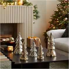 christmas trees are sitting on a table in front of a fireplace and decorated for the holiday season