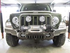 the front end of a green jeep in a garage with two lights on it's headlamps