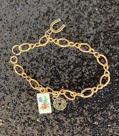 A chain bracelet embellished with small charms to bring the lucky player lots of winning hands A horseshoe, Chinese good luck coin and a mahjong tile hang from these gold toned bracelets  Choose one🀄️🍀❤️ for yourself and gift another to a friend Gold Chain Bracelet With Logo Charm As Gift, Good Luck Charms Bracelet, Vintage Charm Bracelet With Adjustable Chain As Gift, Adjustable Good Luck Charm Bracelet, Metal Charm Bracelet With Logo For Gift, Metal Charm Bracelet With Logo As Gift, Metal Bracelet With Logo Charm As A Gift, Metal Bracelets With Logo Charm As Gift, Metal Jewelry With Logo Charm As Gift