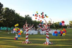 balloons are floating in the air on top of tall trees at an outdoor party with tables and chairs