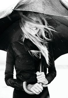 a woman holding an umbrella while standing in the rain with it's wind blowing her hair