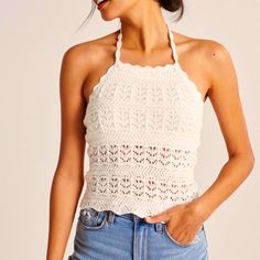 a woman wearing a white crochet halter top and blue jeans with her hands in her pockets