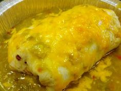 an enchilada covered in melted cheese and green sauce sits in a foil container